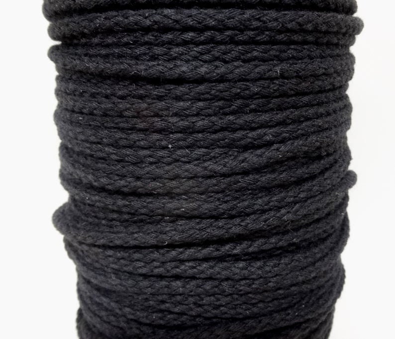 May include: A close-up of a spool of black cotton rope. The rope is tightly wound and has a rough texture.