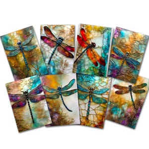 May include: A collection of eight rectangular greeting cards, each featuring a detailed dragonfly illustration set against a vibrant, abstract alcohol ink background with swirling patterns of gold, blue, teal, orange, and purple hues.