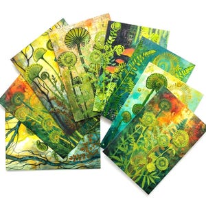 May include: A collection of rectangular greeting cards arranged in a fan shape, each featuring vibrant botanical illustrations of ferns and dandelion-like seed heads in shades of lime green, yellow, orange, and deep teal against textured backgrounds.
