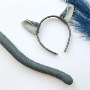 May include: A gray cat tail costume accessory with a matching headband featuring gray felt ears. The headband is made of a brown braided material.