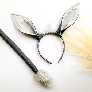May include: A gray and white bunny costume set, including a headband with upright ears and a matching tail. The ears are gray with white interiors, and the tail is fluffy. The set is designed for costume or dress-up play.