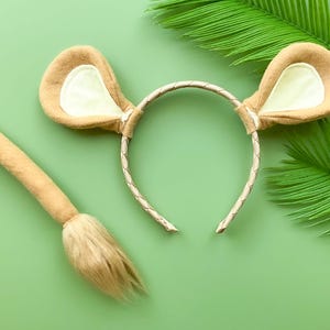 May include: A brown and white lion costume headband with a matching brown and white tail. The headband has a braided gold band and the tail has a fluffy tip.