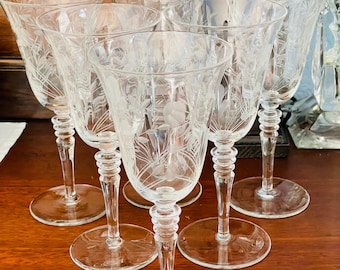 May include: Set of six clear glass wine glasses with etched floral designs. The glasses have a tall, slender stem and a wide bowl.