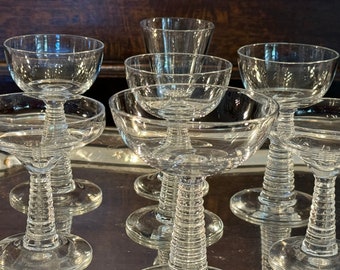 May include: Set of eight clear glass champagne coupes with a unique, textured, spiral stem design. The glasses are arranged on a silver tray.