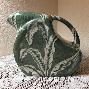 May include: A green ceramic jug with a white leaf pattern. The jug has a rounded body and a handle.