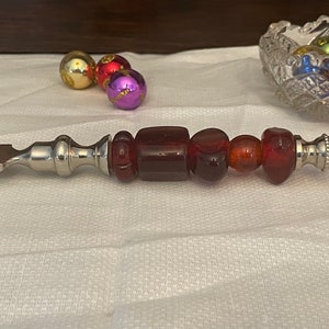 May include: A silver letter opener with a handle made of red and orange glass beads.