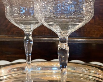 May include: Two clear glass stemmed cocktail glasses with intricate etched designs. The glasses are on a silver tray.
