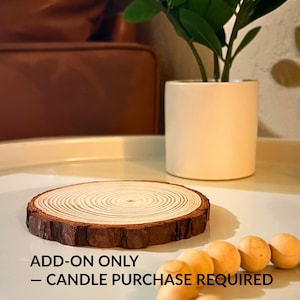 May include: A round, wooden candle base with visible growth rings and a dark brown bark edge. The text "ADD-ON ONLY - CANDLE PURCHASE REQUIRED" is printed at the bottom. Several small, round, light-colored objects are also present.