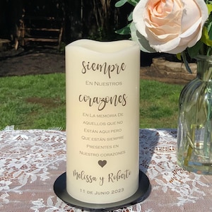 Peut inclure: Une bougie pilier cr&egrave;me avec l'inscription en espagnol "Siempre En Nuestros Corazones". La bougie, pos&eacute;e sur une base noire, pr&eacute;sente un symbole de c&oelig;ur, les noms "Melissa y Roberto" et la date "11 de Junio 2023".