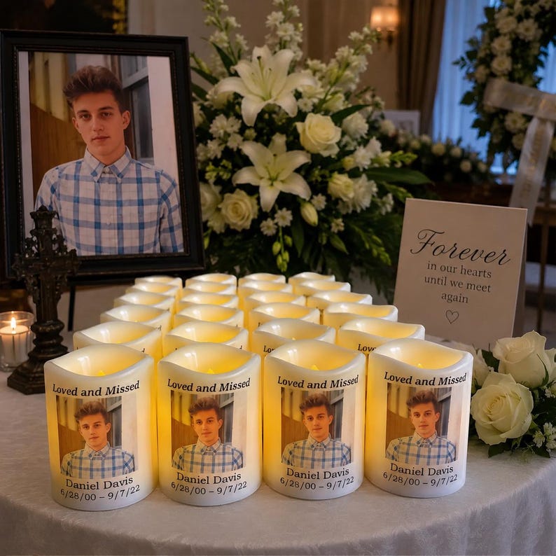 Op de afbeelding: Een verzameling cilindervormige LED-herdenkingskaarsen met een foto van een jong persoon in een blauw geruit overhemd. Elke kaars is bedrukt met de tekst Loved and Missed, de naam Daniel Davis en de data 6/28/00 - 9/7/22.
