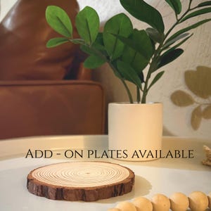 Peut inclure: Une tranche de bois ronde avec des anneaux de croissance visibles et un bord en &eacute;corce brun fonc&eacute;. Le texte "ADD - ON PLATES AVAILABLE" est affich&eacute;. Une petite plante en pot et des perles en bois sont &eacute;galement visibles.