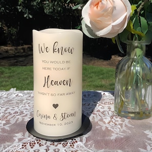 Peut inclure: Une bougie pilier cr&egrave;me avec le texte "We know, You would be here today if Heaven wasn't so far away." La bougie comprend les noms "Corina & Steven" et la date "November 10, 2023." La bougie repose sur une plaque noire.