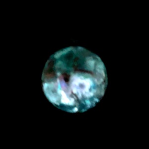 May include: A round, iridescent object with a dark background. The object has a mix of blue, green, and purple hues, with a textured surface. The overall shape is spherical, and the lighting creates highlights and shadows.