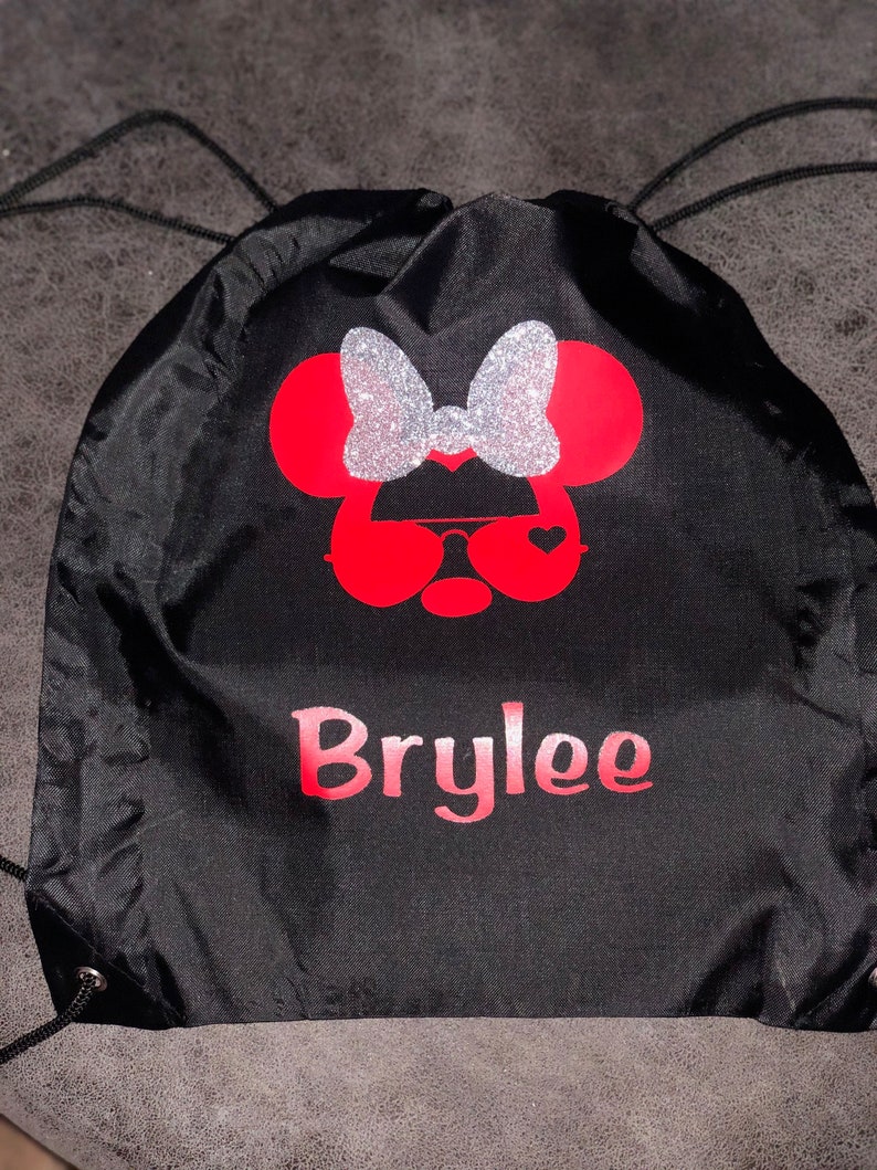 May include: Black drawstring bag with a red and silver glitter Minnie Mouse design and the name "Brylee" printed in pink.