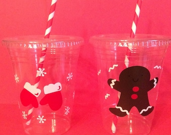May include: Two clear plastic cups with red and white striped straws. One cup has a red mitten design and the other has a gingerbread man design.