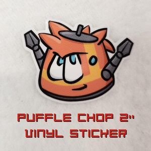 May include: A 2-inch vinyl sticker featuring a cartoon robot with orange, yellow, and gray colors. The robot has large eyes and a mischievous expression. The sticker says "PUFFLE CHOP 2" in a pixelated font.