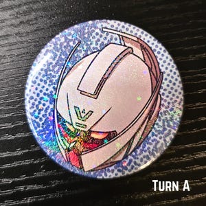 Puede incluir: Bot&oacute;n redondo con un dise&ntilde;o hologr&aacute;fico y brillante. El bot&oacute;n presenta una ilustraci&oacute;n blanca y rosa de una cabeza de robot con el texto "TURN A" en la parte inferior. El fondo es azul claro con peque&ntilde;os puntos.