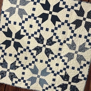 Puede incluir: Un edredón hecho a mano con un patrón repetido de estrellas en azul marino y crema. El edredón presenta costuras intrincadas y un diseño de patchwork, creando un textil acogedor y decorativo. El edredón está hecho de tela.