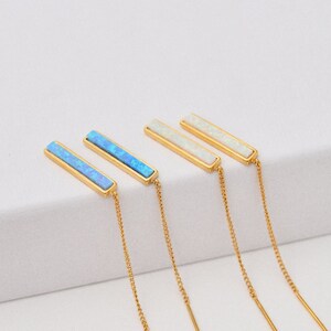 May include: Two pairs of gold-tone threader earrings. One pair features rectangular bars with bright blue inlay, while the other pair features rectangular bars with white inlay. Each earring consists of a thin gold chain attached to the bar.