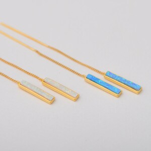 May include: Two pairs of gold-tone threader earrings. One pair features rectangular white opal-like inlays, while the other pair features rectangular blue opal-like inlays. Each earring consists of a thin gold chain attached to a metal bar setting.