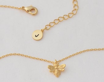 May include: A gold chain necklace with a small bee charm and a circular pendant with the letter 'J' inscribed on it.