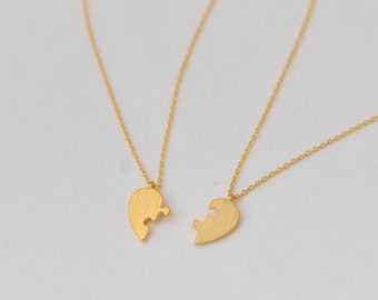 May include: Two gold necklaces with matching heart-shaped pendants. The pendants are designed to fit together like puzzle pieces.