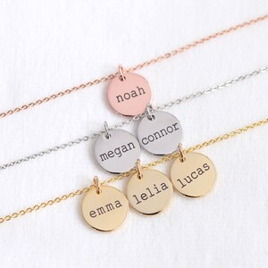 Op de afbeelding: Vijf gouden kettingen met ronde hangers, elk gegraveerd met een andere naam: Emma, Lelia, Lucas, Megan en Connor. De bovenste ketting heeft een ros&eacute;gouden ketting en een hanger gegraveerd met de naam Noah.