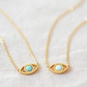Könnte beinhalten: Zwei goldene Halsketten mit einer zarten Kette und einem Augen-Anhänger. Der Augen-Anhänger hat einen kleinen Opal-Stein in der Mitte. Ein Anhänger hat einen hellblauen Opal und der andere einen weißen Opal.