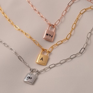 May include: Three gold, silver, and rose gold necklaces with padlock pendants. The padlocks are engraved with the letters "A", "M&J", and an infinity symbol.
