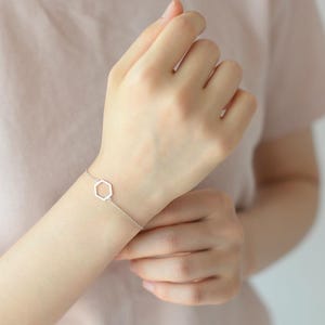 May include: A silver bracelet with a geometric hexagon charm. The bracelet is delicate and simple, perfect for everyday wear.