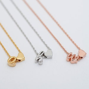 Pode incluir: Três colares delicados com um pingente de coração e um pingente de letra. Os colares são de ouro, prata e ouro rosa.