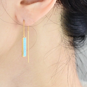 May include: A gold threader earring featuring a thin, vertical rectangular pendant inlaid with a bright turquoise stone. The earring consists of a delicate gold chain that passes through the earlobe, ending in a straight, slender gold post.