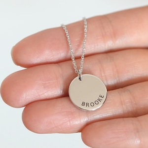 Puede incluir: Collar de plata con un colgante redondo que dice "BROOKE".
