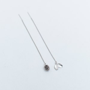 May include: A pair of silver dangle earrings with a pine cone charm on one earring and two leaf charms on the other.