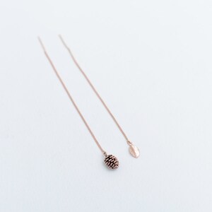 May include: A pair of rose gold dangle earrings with a pine cone and leaf charm.