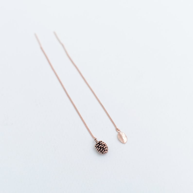 May include: A pair of rose gold dangle earrings with a pine cone and leaf charm.