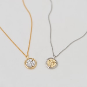 May include: Two gold necklaces with a spinning coin pendant. The coin features a raised design of a person holding a lightning bolt. One necklace has a gold chain and the other has a silver chain.