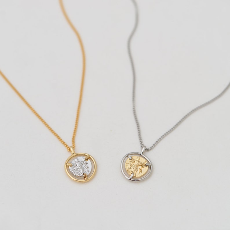 May include: Two gold necklaces with a spinning coin pendant. The coin features a raised design of a person holding a lightning bolt. One necklace has a gold chain and the other has a silver chain.