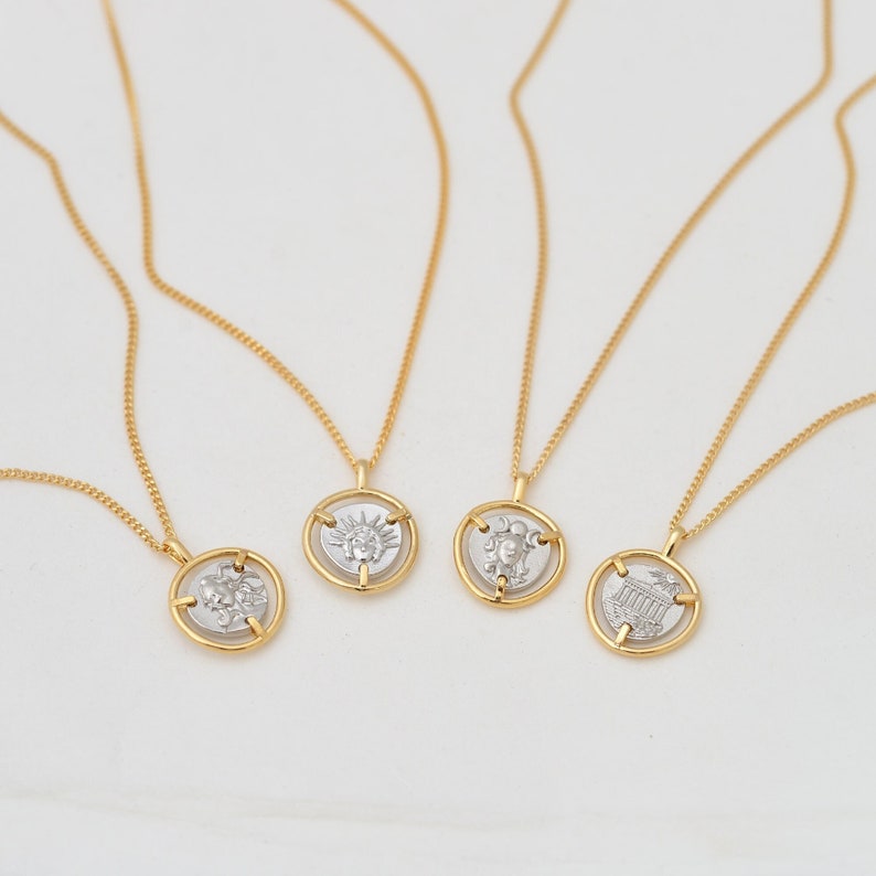 May include: Four gold necklaces with silver coin pendants featuring different designs. The coins are framed in a gold circle with four gold bars.