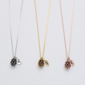 Può includere: Tre delicate collane con un ciondolo a forma di pigna e un ciondolo con iniziale personalizzata. Le collane sono disponibili in argento, oro e oro rosa.