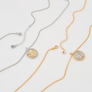 May include: Three gold necklaces with a coin pendant. The coins feature a sun design, a face, and a figure. The necklaces are on a white background.