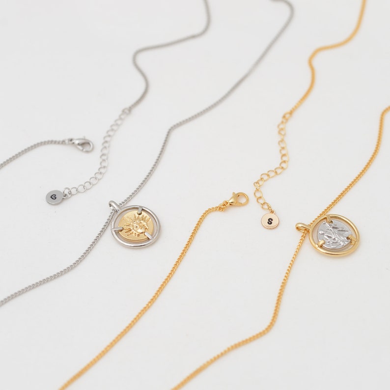 May include: Three gold necklaces with a coin pendant. The coins feature a sun design, a face, and a figure. The necklaces are on a white background.