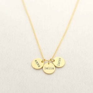 Op de afbeelding: Gouden ketting met drie ronde bedels, elk gegraveerd met een naam: Emma, Lelia en Lucas.
