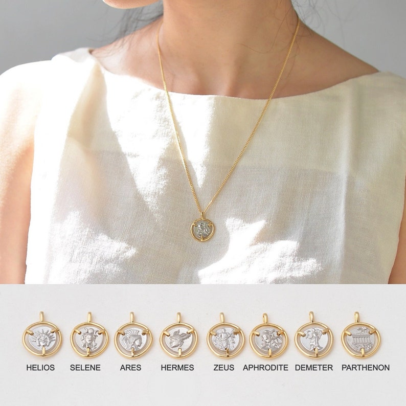 May include: Gold chain necklace with a silver coin pendant featuring a Greek god or goddess. The pendant is surrounded by a gold frame.  The necklace is displayed on a white background with eight different coin pendants below, each with a different Greek god or goddess. The coin pendants are labeled with the names of the gods and goddesses: Helios, Selene, Ares, Hermes, Zeus, Aphrodite, Demeter, and Parthenon.