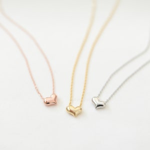 Puede incluir: Tres delicados collares con pequeños colgantes en forma de corazón. Los collares son de oro rosa, oro y plata.