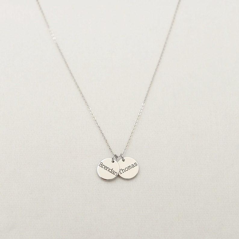 Op de afbeelding: Zilveren ketting met twee ronde hangers, een gegraveerd met "Brendan" en de andere met "Thomas".