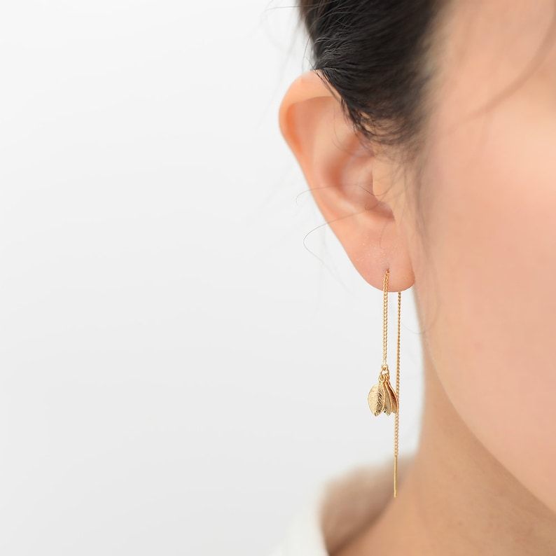 May include: Gold chain earrings with three small gold leaf charms dangling from the bottom.