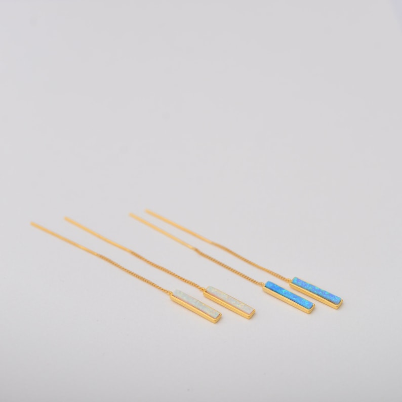 May include: Two pairs of gold-tone threader earrings. One pair features rectangular white opal-like inlays, while the other pair features rectangular blue opal-like inlays. Each earring consists of a thin gold chain attached to a metal bar setting.