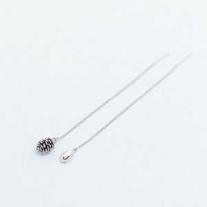 May include: A pair of silver dangle earrings with a pine cone charm on one side and a leaf charm on the other.