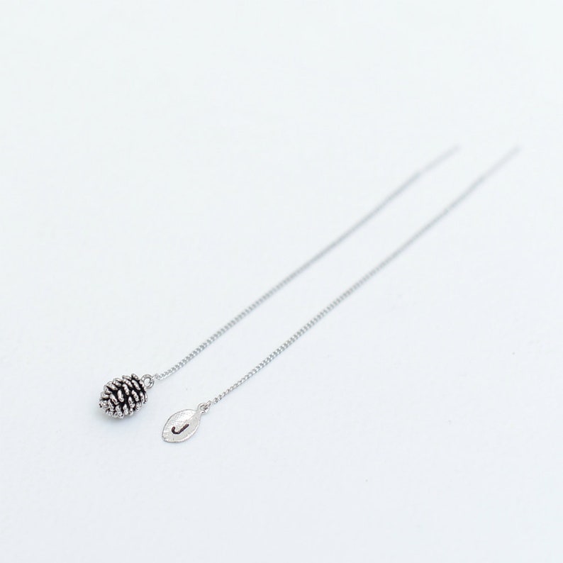 May include: A pair of silver dangle earrings with a pine cone charm on one side and a leaf charm on the other.